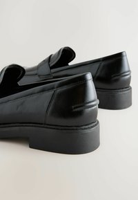 Mustat nahka loaferit, joissa on sileä pinta, pyöristetty kärki, matala lohko korko ja hienovarainen ompelu yksityiskohtana sivuilla. Yksinkertainen muotoilu.