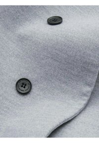 Tessuto di lana grigia con una consistenza morbida, caratterizzato da un bottone nero ben in evidenza. Il materiale è liscio, con sottili variazioni di tonalità.