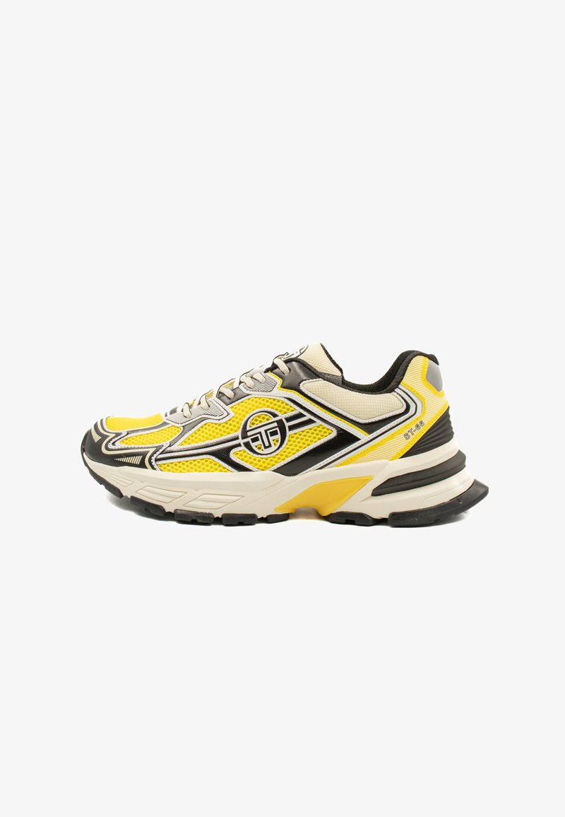 Sportcipő, amelynek főként sárga textil felsőrésze van, fekete kiegészítőkkel, textúrázott hálós részletekkel és egy szürke alapú párnázott talppal.