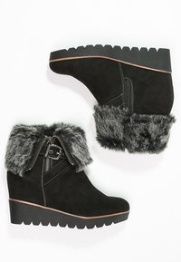 Černé semišové kotníčkové boty s šedým umělým kožíškem na horním okraji, detaily se zipem a silnou strukturovanou klínovou podrážkou. Obsahuje kontrastní švy.