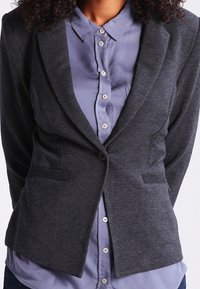 Gray structured blazer with notch lapels, two front pockets, and a single-button closure, worn over a light blue button-up shirt.