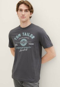 Graues Baumwoll-T-Shirt mit türkisfarbenem Text, der den Markennamen, das Gründungsjahr und "Premiumqualität" anzeigt. Mit kurzen Ärmeln und Rundhalsausschnitt.
