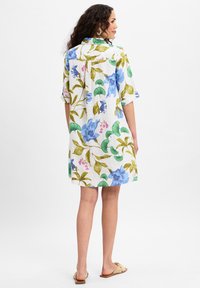 Witte linnen jurk met een kleurrijk bloemenpatroon in blauw, groen en roze accenten. Korte mouwen, knoopsluiting aan de achterkant en een relaxte pasvorm.