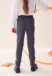 Grijze broek met een gladde textuur, een getailleerd ontwerp en een achterzak. Gecombineerd met zwarte schoenen. Simpele en functionele stijl.