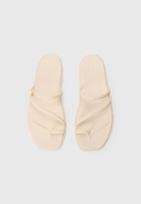 Beige slide sandals with a flexible design. Two thin straps cross over the foot, flat sole with slight texture and rounded edges.
