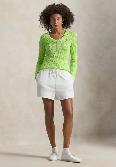 Φούτερ πλεκτό με καλώδιο σε νέον πράσινο χρώμα, με V-λαιμόκοψη και μικρό λογότυπο, συνδυασμένο με λευκά σορτς με κορδόνι και λευκά αθλητικά παπούτσια.