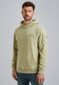 Felpa verde chiaro, materiale in cotone, vestibilità rilassata, tasca frontale, polsini e orlo a coste, logo ricamato sul petto, toppa discreta sulla spalla.