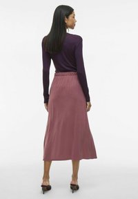 Jupe longue rose avec une taille élastique, associée à un haut violet ajusté à manches longues. Texture de tissu lisse, longueur mi-mollet.