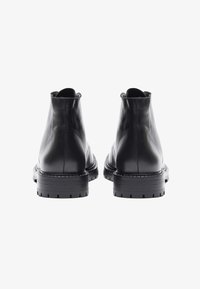 Botas de cuero negras de tobillo con una textura suave, puntera redondeada y suela de goma reforzada con ranuras horizontales.