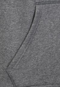 Pohled zblízka na šedou mikinu s velkou kapsou, která ukazuje měkkou textura a rovnoměrný pletený vzor. Jsou viditelné šité okraje.