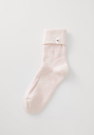 Lys rosa foldet kalv-længde sok med en lille hvid label med "cK" nær manchetten, på en ensfarvet hvid baggrund.