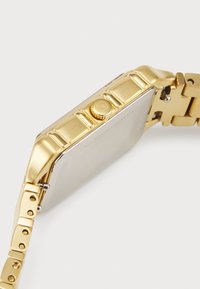 Goldfarbene Edelstahl-Uhr mit einem rechteckigen Gehäuse, strukturiertem Gliederarmband und einer seitlichen Krone für Anpassungen.