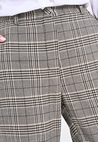 Grau-beige karierte Hose aus strukturiertem Stoff, mit einem klassischen Karomuster, seitlichen Taschen und einer taillierten Passform.