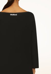 Sort top med bred, rund halsudskæring og lange ærmer. Har et lille, hvidt "Wolford"-logo på ryggen. Glat tekstur.