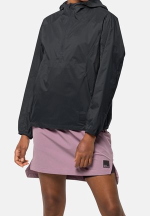 Osoba ubrana w czarną bluzę z kapturem oraz jasnofioletową spódnicę z małą naszywką z logo na dolnym brzegu.