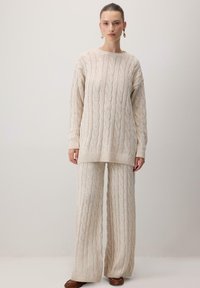 Pehmeä neulepusero ja väljät housut luonnonvalkoisena. Teksturoitu kangas, ribattu hihansuu ja helma. Rentouttava malli, minimaalinen muotoilu ja neutraali väri.