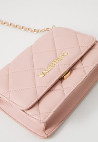 Rosa kviltad läderhandväska med en guldkedjesadel, prydd med en guldfärgad "Valentino"-logotyp och en säker låsning.
