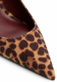 Zapato de tacón alto con estampado de leopardo y punta afilada, fabricado en un material suave y texturizado, con manchas marrones y negras sobre un fondo beige.