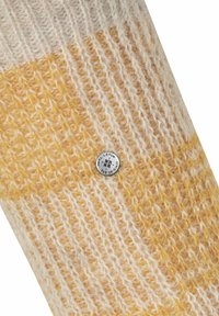 Die gestrickte Wollsocke hat ein Muster aus elfenbeinfarbenen und gelben Streifen, mit einer strukturierten Oberfläche und einem silbernen Logo-Button, der an der Seite eingeprägt ist.