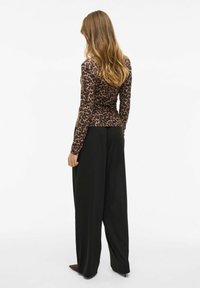 Halenka s leopardím potiskem s dlouhým rukávem, spárovaná s volnými černými kalhotami, které mají hladkou texturu a obepnutý pas.