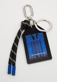 Kulcstartó, amelyen egy fekete és kék címke található, rajta az "OUT OF THE BLUE" felirat, szőtt fekete és fehér zsinórra és ezüst fém gyűrűre erősítve.