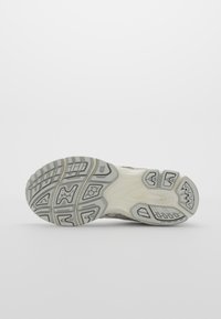 Semelle de chaussure avec motif gris et blanc montrant une adhérence texturée et des détails de coussinage sur un fond clair uni.