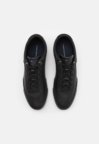 Černé syntetické kožené tenisky s hladkým povrchem, plochými tkaničkami, kulatou špičkou a diskrétními logovými akcenty na stélce.