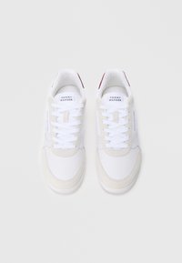 Pár bílých tenisek Tommy Hilfiger s béžovými semišovými detaily a bílými tkaničkami na jednoduchém světlém pozadí.