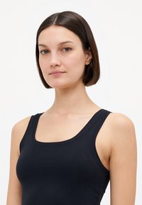 Black tank top featuring a square neckline and wide straps, made of smooth, stretchy fabric, designed for a fitted look.