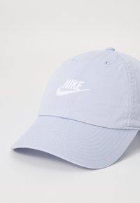 Svetlofialová bavlnená baseballová čiapka s bielou vyšitou ikonou Nike na prednej strane. Obsahuje zakrivený šilt a ventilačné otvory.