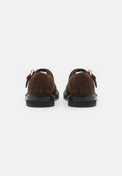 Pantofi din suede maro cu vârf rotund, talpă din cauciuc negru și un funda decorativă pe toc. Textură netedă cu elemente de design minime.
