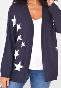 Tmavě modrý kardigan s bílými hvězdnými vzory, otevřený přední design, dlouhé rukávy a žebrované manžety, vyrobený z měkkého pleteného materiálu.