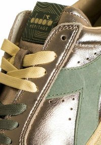 Sneaker in pelle scamosciata verde e argento metallico con lacci gialli e oliva, dotata di dettagli testurizzati e forature sui lati.