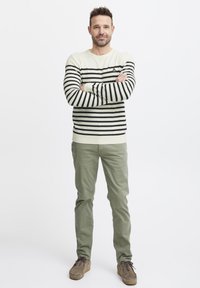 Vaalean kerma sweater, jossa on mustia vaakasuoria raitoja, muotoiltu malli. Oliivinvihreät housut, pehmeä tekstuuri ja ruskeat nauhakengät.
