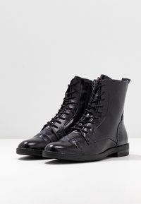 Bottes noires à talon en cuir texturé avec une finition lisse, dotées de lacets, de fermetures éclair latérales et d'un design de bout arrondi.