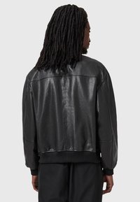 Fekete bőr bomber dzseki bordás mandzsettával és aljjal. Simás textúra, oversized fazon és letisztult design, látható záróelemek nélkül.