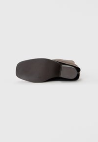 Black rubber sole with a textured surface and a gradual curve, accompanied by a brown upper made of soft material.