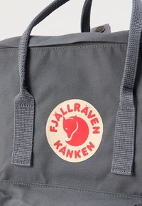 Γκρι σακίδιο πλάτης από ύφασμα με διπλές υφαντές λαβές, κυκλικό λογότυπο με σχέδιο κόκκινου αλεπού και το όνομα της μάρκας «FJÄLLRÄVEN KÅNKEN».