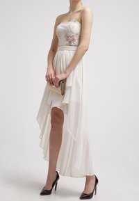 Häikäisevä hartiaton ivory-mekko, jossa on kukkakirjailtu yläosa ja epäsymmetrinen helma, valmistettu kevyestä kankaasta. Yhdistetty kultaisiin clutch-laukkuun ja tummiin korkokenkiin.