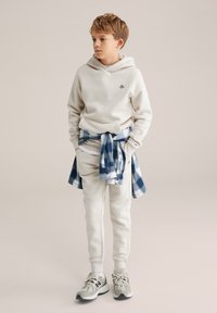 Valkoinen huppari, jossa on pieni logo, yhdistettynä saman sävyisiin kapeneviin housuihin. Vyötärölle sidottu sininen ruudullinen paita. Neutraalit tennarit viimeistelevät asun.