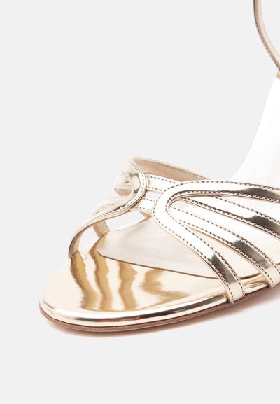 Χρυσό μεταλλικό ανοιχτό πέδιλο με πολλαπλούς λεπτούς ιμάντες και μικρό υφασμάτινο μαξιλάρι στη σόλα, τοποθετημένο σε απλό λευκό φόντο.