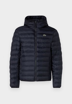 Marineblå polstret jakke med hætte, der har en frontlynlås og elastiske manchetter. Teksturfinish med vandret søm og en logo accentering.