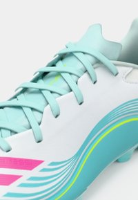 Hvit fotballsko med akvatiske og rosa aksenter, med glatt design og teksturerte lisser. Merkbare buede linjer langs siden.
