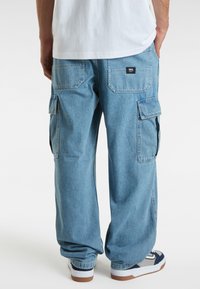 Pantaloni cargo in denim azzurro chiaro con doppie tasche laterali, tasche posteriori a toppa e una vestibilità rilassata. Abbinati a sneakers bianche e blu navy.