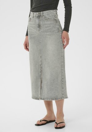 Gonna midi in denim grigio con cucitura verticale, vita alta e leggera scoloritura. Presenta una chiusura con cerniera e orlo cucito. Sandali neri a infradito visibili.