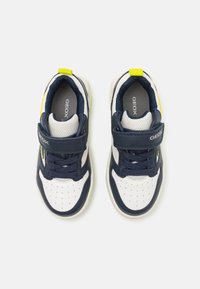 Navy and white sneakers with mesh panels, a Velcro strap, and contrasting yellow accents. Features perforated toe for breathability.