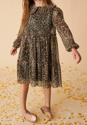 Robe imprimé léopard avec un design plissé, manches longues et col à volants ; associée à des ballerines roses brillantes sur un sol couvert de confettis.