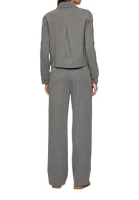 Grijze katoenen jas met een kraag en een rugplooi, gecombineerd met bijpassende wijde broek. De broek heeft twee achterzakken en subtiele stikdetails.