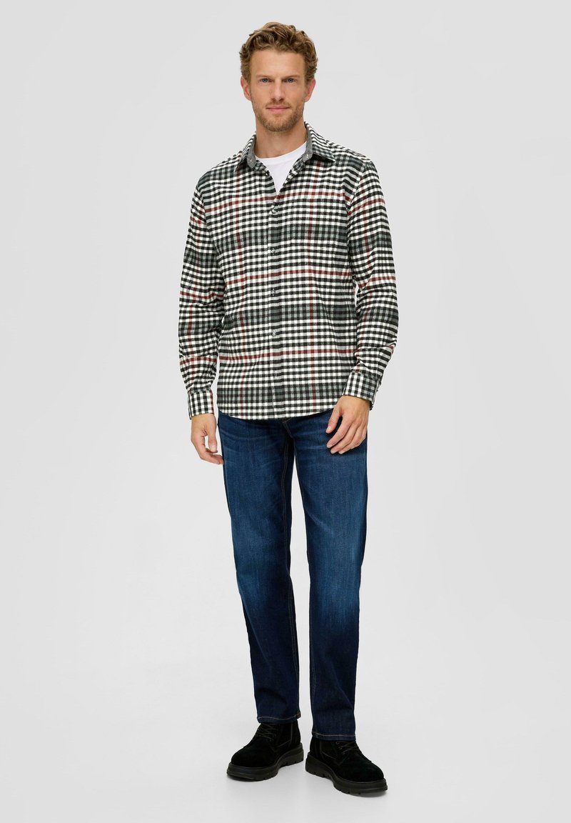 Koszula flanelowa z czarno-biało-czerwonym wzorem w kratę, z długimi rękawami i zapięciem na guziki, połączona z niebieskimi dżinsami i czarnymi butami.