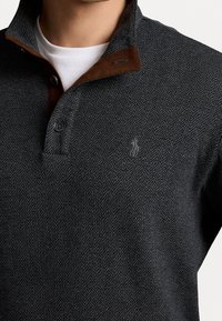 Dunkelgrauer Pullover mit Fischgrätmuster, braunem Wildlederkragen, zwei Knöpfen und einem kleinen gestickten Logo auf der linken Brust.